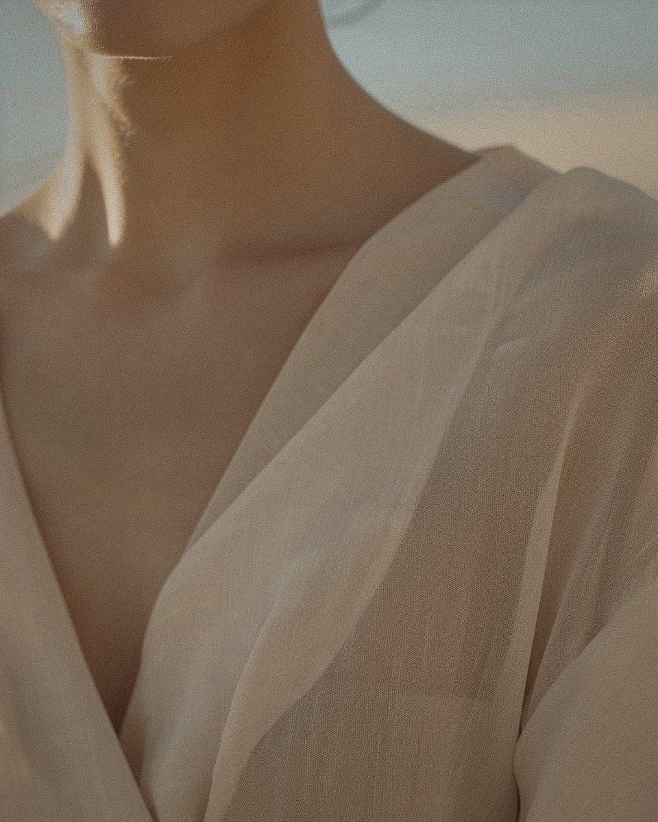 The neck and shoulder of a woman in a soft white robe, lit low and warm
