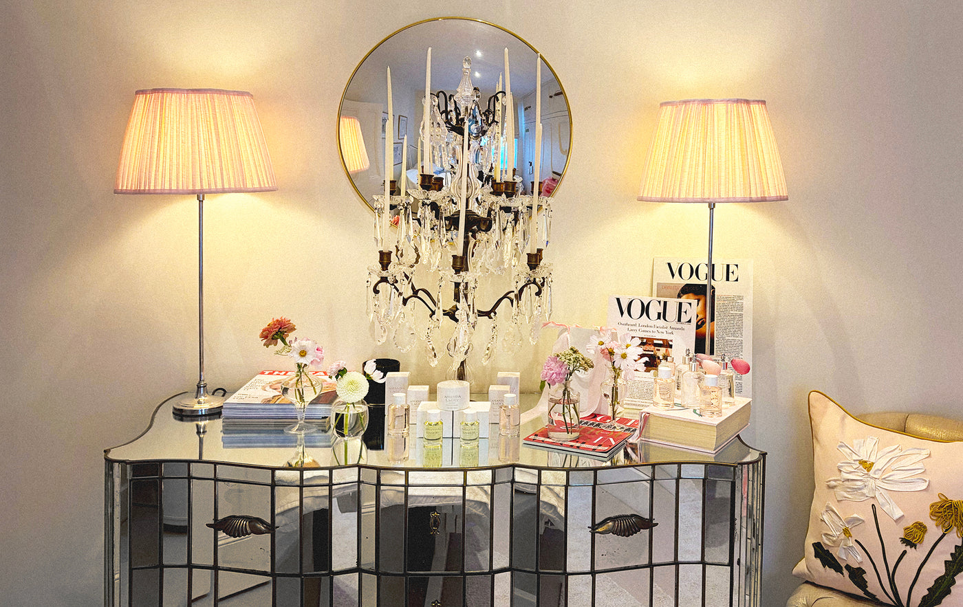 The Amanda Lacey atelier: a mirrored console under a crystal candelabra, her formulations and press laid out beside pink silk lampshades
