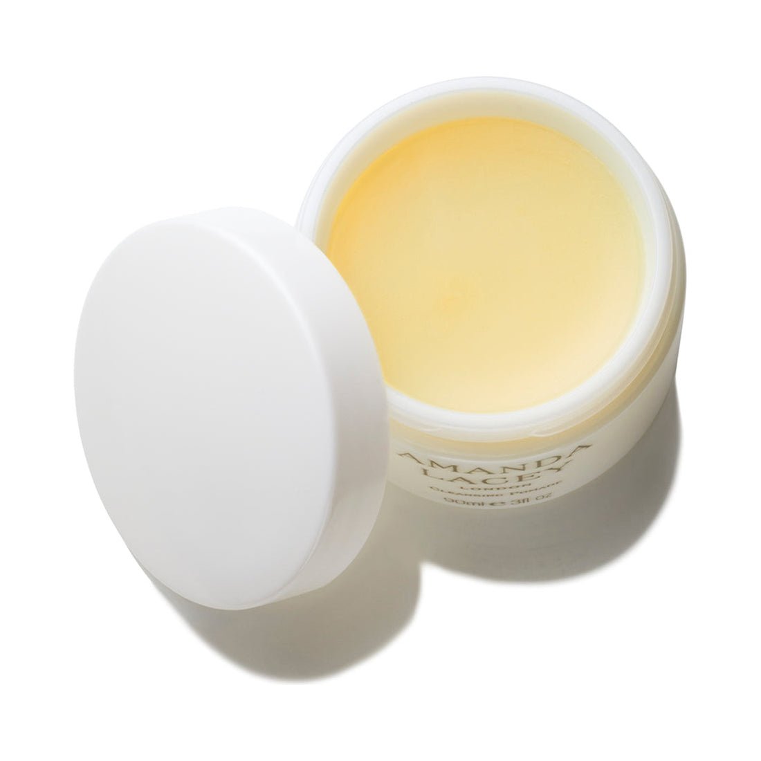 Amanda Lacey Cleansing Pomade, open white glass jar of pale golden balm with lid beside it